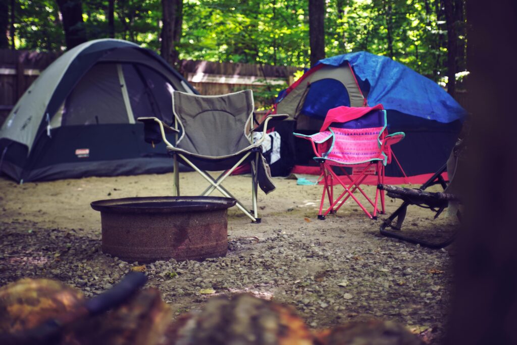 A serene campsite in the woods with colorful tents, camping chairs, and a fire pit, perfect for a leisure getaway.