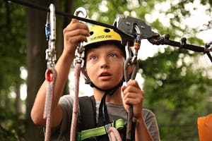 A young boy enjoying a rope climbing activity outdoors, wearing a helmet and using safety gear.