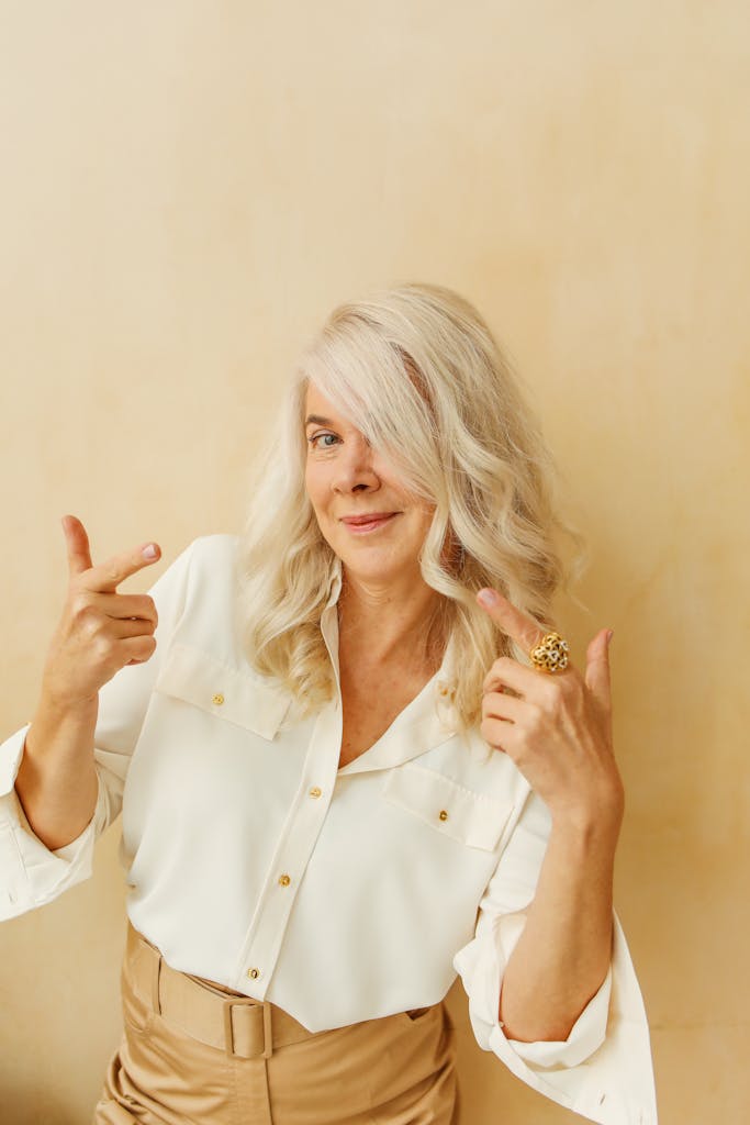 Elegant senior woman with white hair smiling and posing confidently against a neutral background.