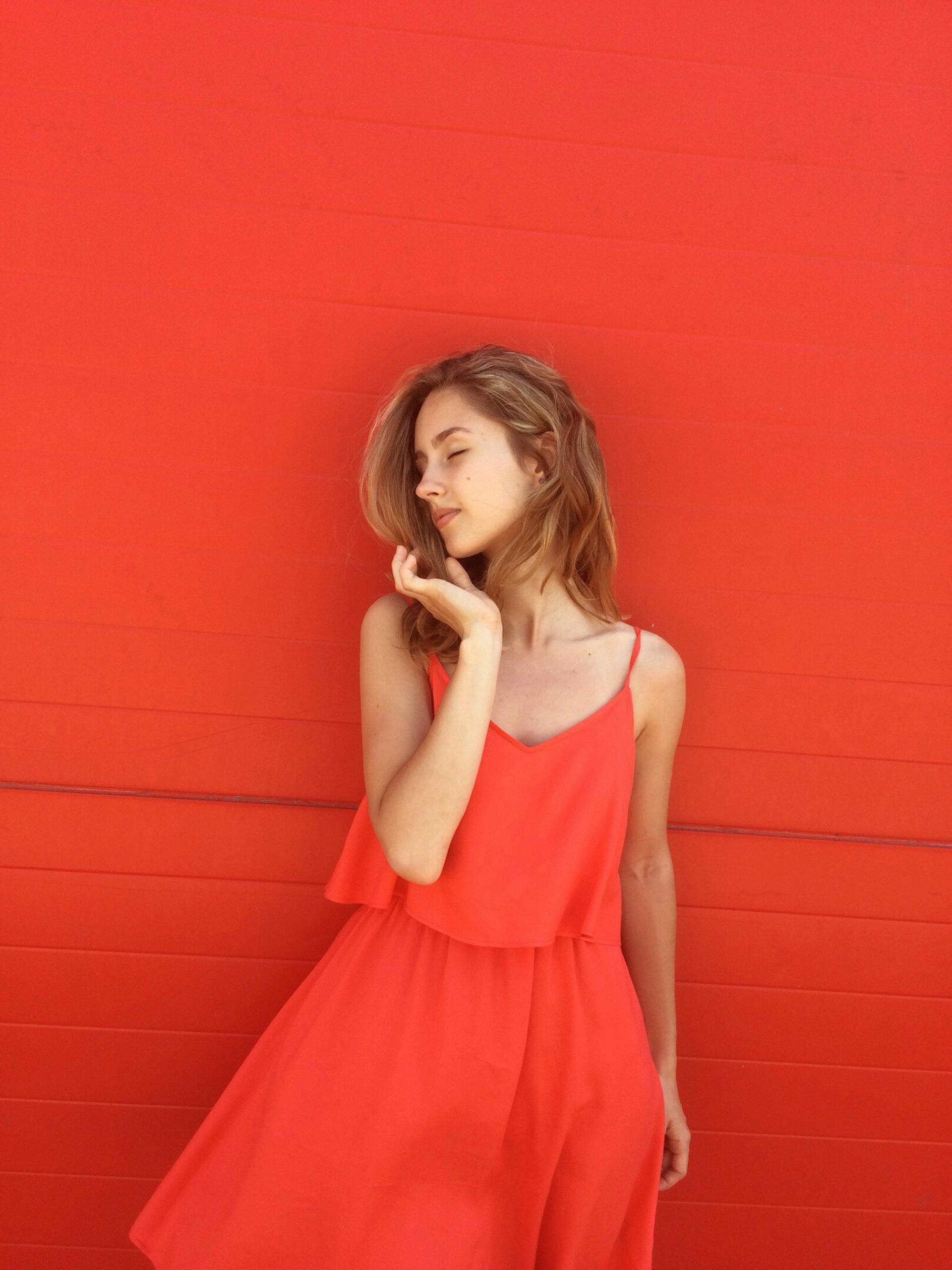 Portrait of a young woman wearing a stylish red dress, posing gracefully against a matching red background.